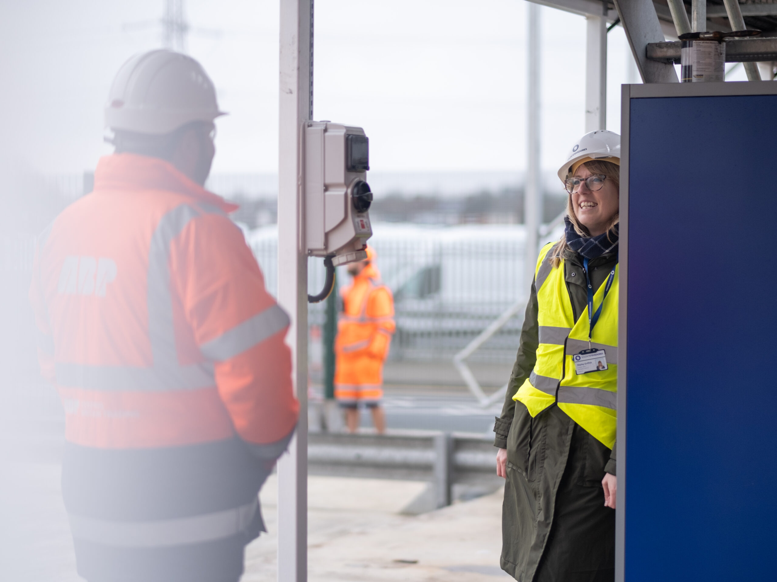 Hayley standing on a gantry wearing PPE  chatting to a client briefing him on an interview