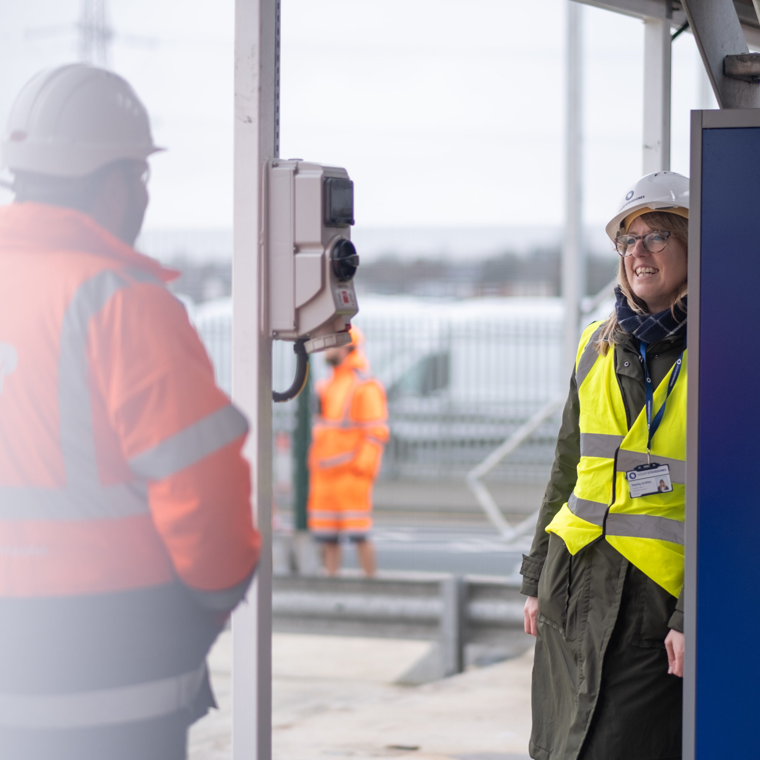 Maritime PR and communications - Woman in high vis holding a microphone between her and the male interviewee. both with their heads turned towards the rail track in the background